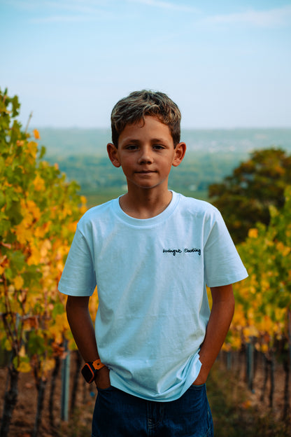 Junge im weißen T-Shirt mit gesticktem Schriftzug „Weingut Eberling“, Hände in den Hosentaschen, zwischen herbstlichen Rebzeilen