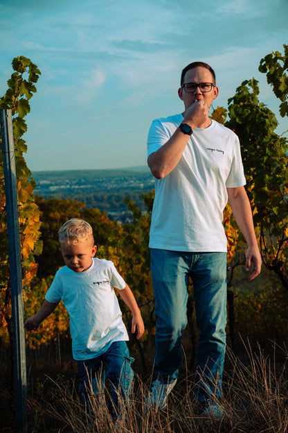 Mann und kleiner Junge in weißen „Weingut Eberling“-T-Shirts laufen durch den Weinberg, im Hintergrund der Blick ins Land