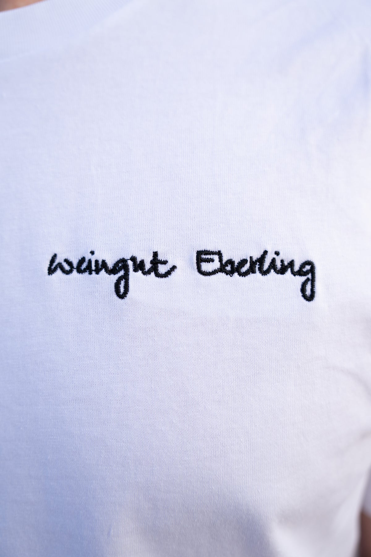 Nahaufnahme der Stickerei: Schriftzug „Weingut Eberling“ in schwarzer Schreibschrift auf weißem T-Shirt-Stoff